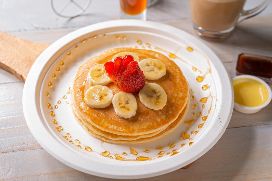 Pila de Pancakes servidos en plato con miel y fresas